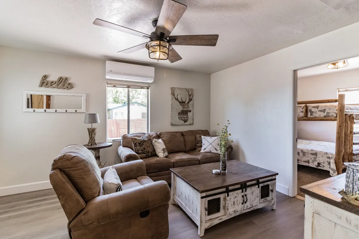 A cozy living space with a comfortable couch, rustic wooden coffee table, and warm natural light streaming through a window. Decorative wall art adds a personal touch, and the overall vibe is inviting and homely.