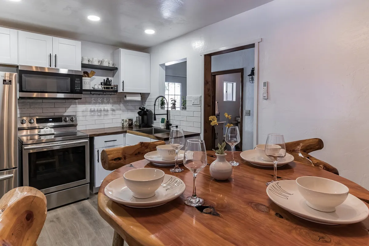 A warm dining area featuring a rustic wooden table set with dishes, surrounded by modern kitchen appliances and wooden accents. The space exudes a welcoming ambiance, ideal for shared meals and celebrations.