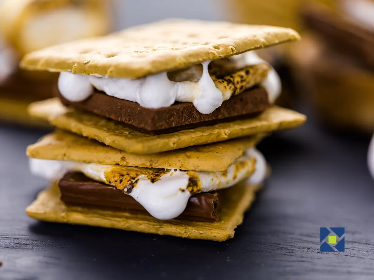 The image features a cozy, inviting interior scene centered around a plate stacked high with freshly made s'mores, surrounded by toasted marshmallows, chocolate bars, and graham crackers, conjuring memories of family gatherings and fireside treats. The arrangement invites guests to imagine the warmth and joy of sharing sweet moments with loved ones in a comfortable cabin setting.