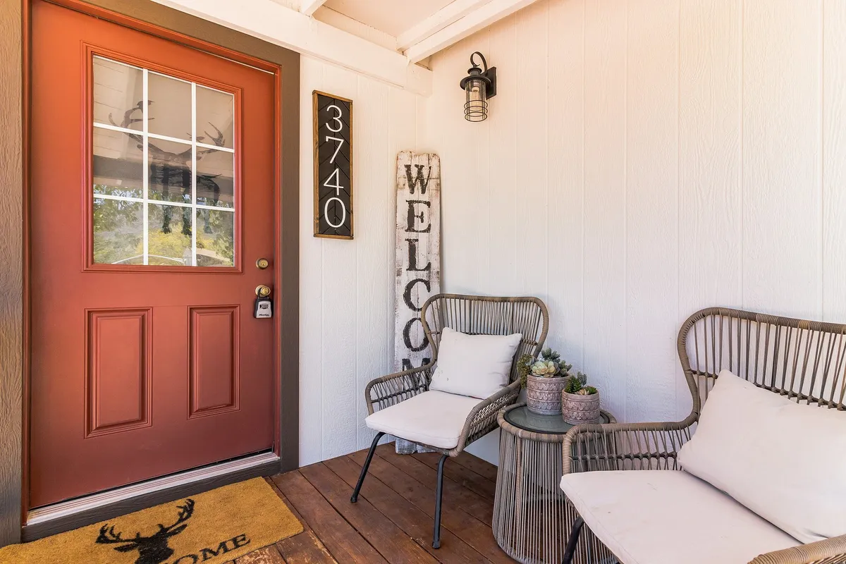 The front entrance of the cabin, showcasing a bright red door, a welcoming sign, and comfortable outdoor seating. The setup conveys a sense of arrival and hospitality, inviting guests to step in and start their outdoor adventure.