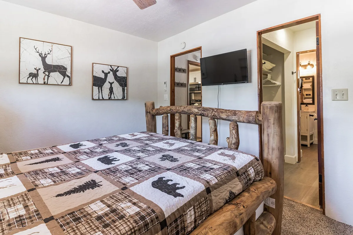 A welcoming master bedroom featuring a rustic log bed frame, decorative wall art, and a flat-screen TV. The room is softly lit, evoking warmth and relaxation, and perfectly illustrates a comfortable and restful retreat after a long day.