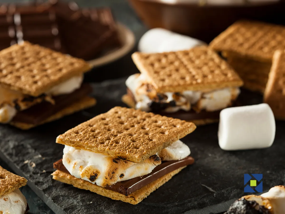 A close-up view of classic s'mores ingredients—marshmallows, chocolate bars, and graham crackers—arranged as if ready for a campfire gathering. The inviting setup suggests outdoor fun and shared moments by the fire.
