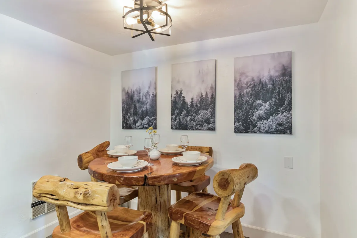 A welcoming dining space with a rustic wooden table, unique wooden chairs, landscape wall art, and a set table. The scene radiates warmth and encourages family meals and memory-making.