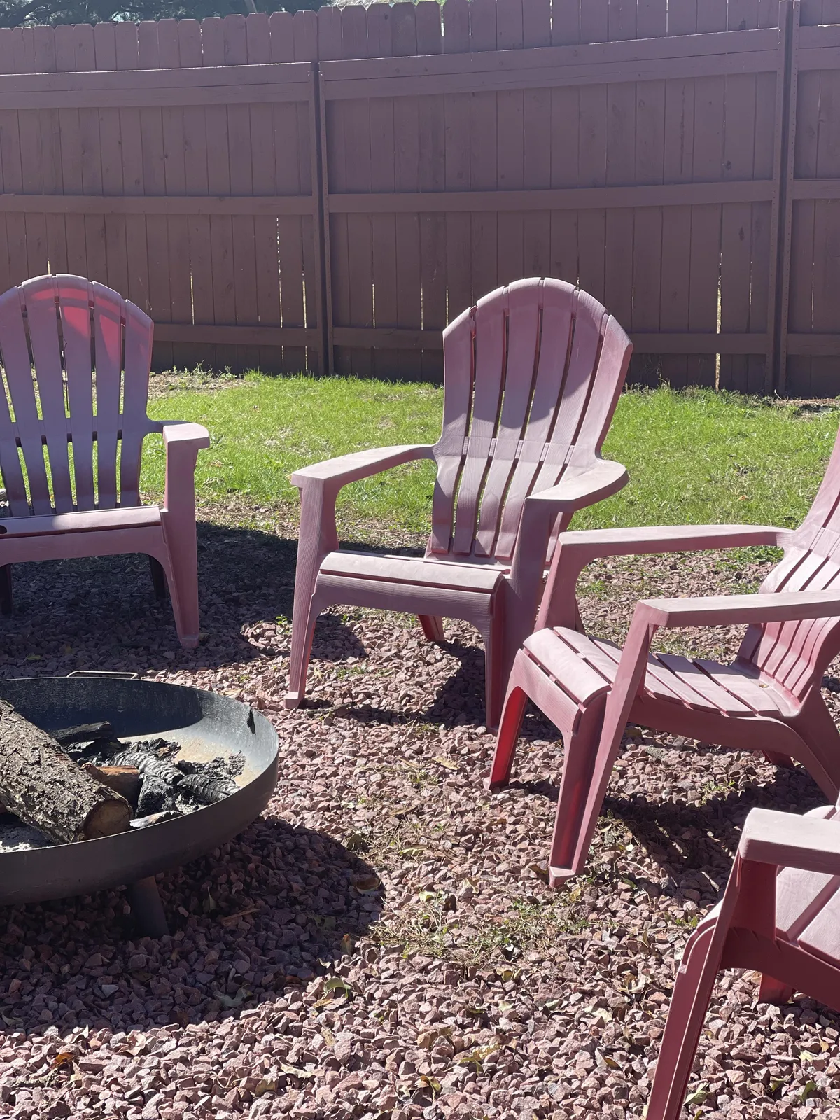 This scene captures a cozy nook with pink Adirondack chairs encircling a fire pit on gravel, set against a natural backdrop. The image invites viewers to imagine stargazing or roasting marshmallows after dark.