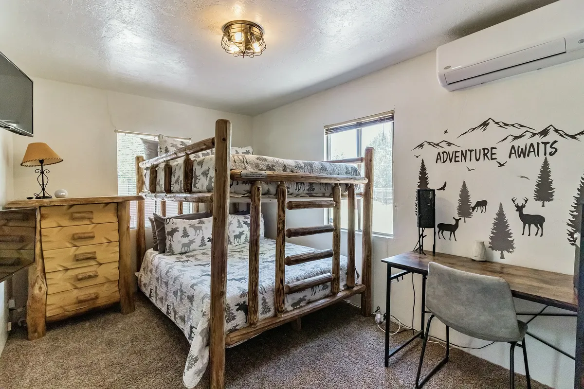 A cozy bunk bed area with wooden dresser, inspirational wall art, and a desk with a chair. The window offers nature views, while the decor hints at an adventurous, family-friendly environment.