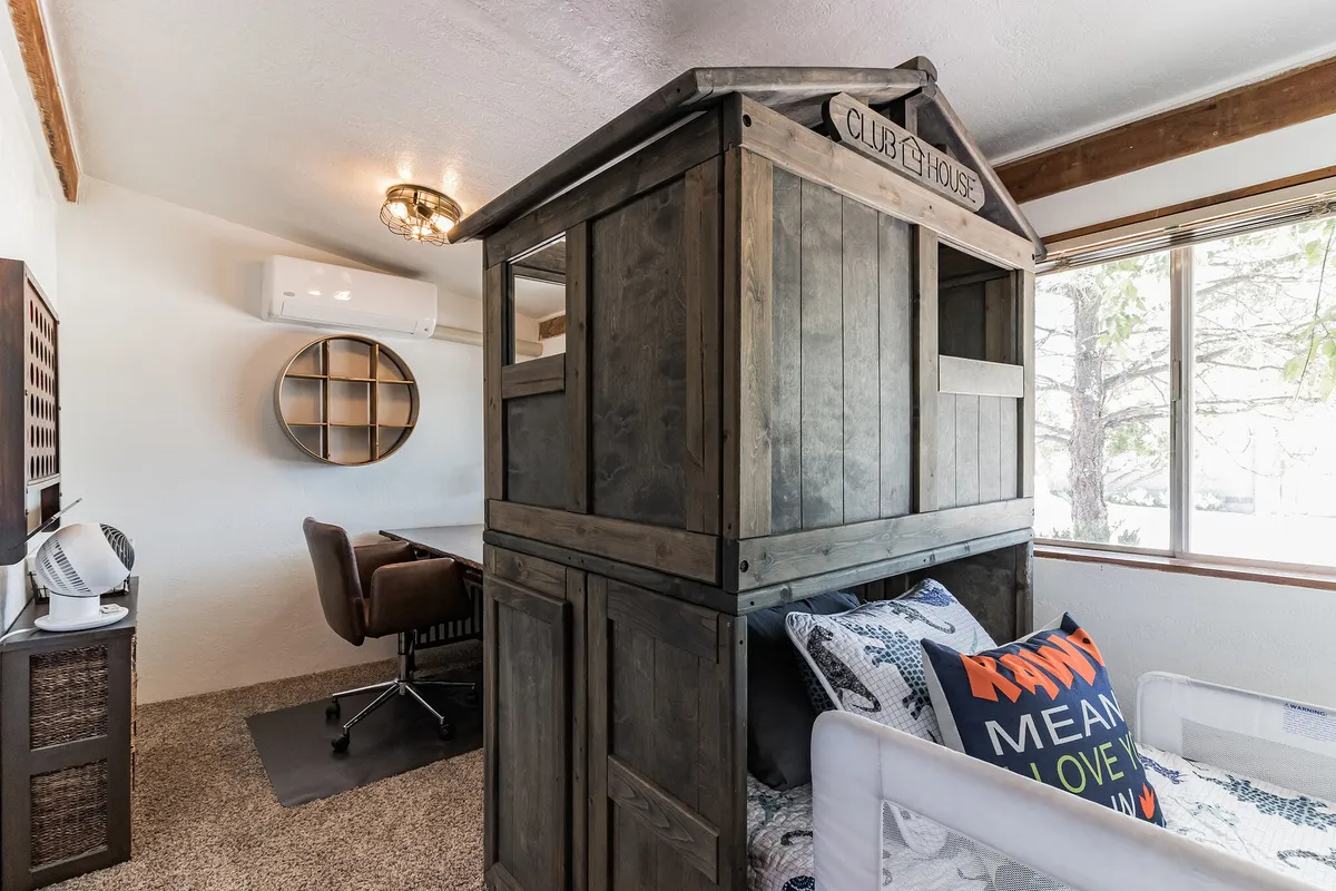 A playful kids’ room with a unique playhouse structure, workspace area, and colorful decorative pillows. The room feels lively and creative, offering both play and study space for younger guests.